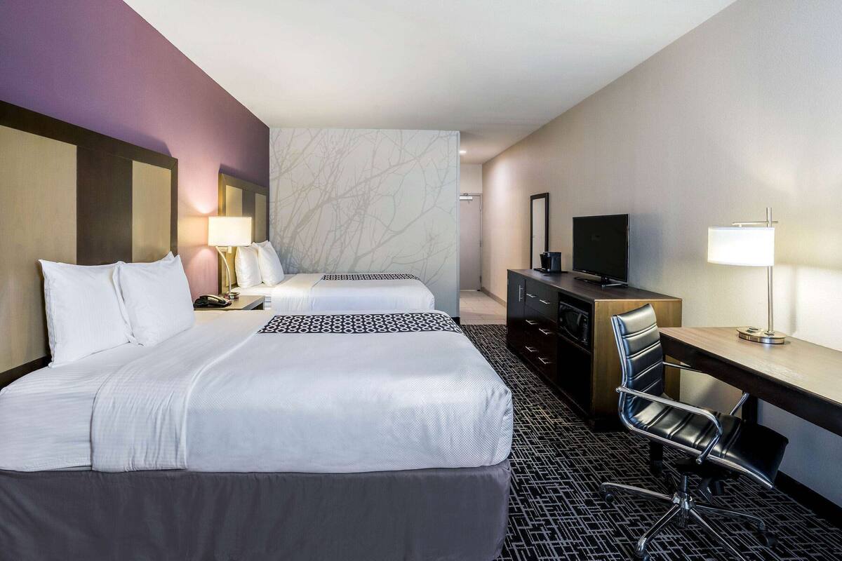 Une chambre d’hôtel avec deux lits, un bureau, une chaise, une télévision et une lampe.