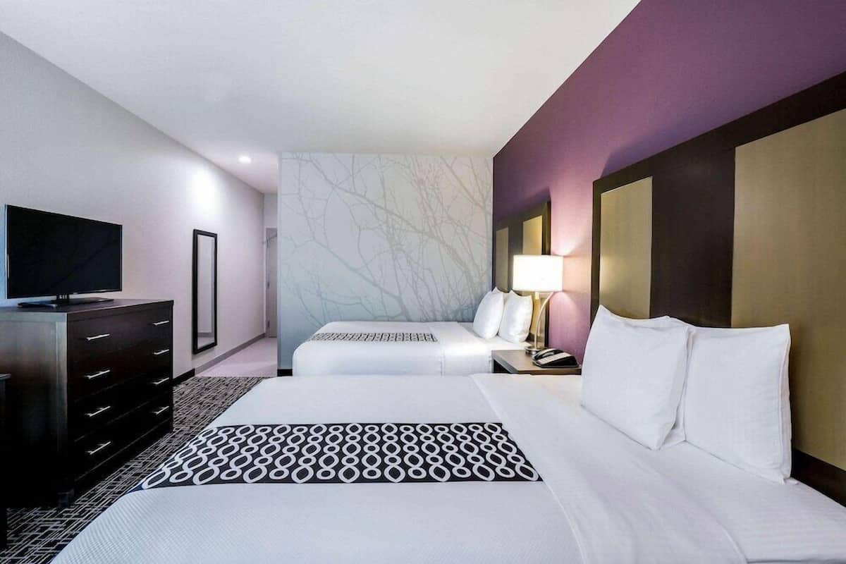 Une chambre d’hôtel équipée d’un lit, d’une télévision, d’une commode et d’une table de chevet avec une lampe.