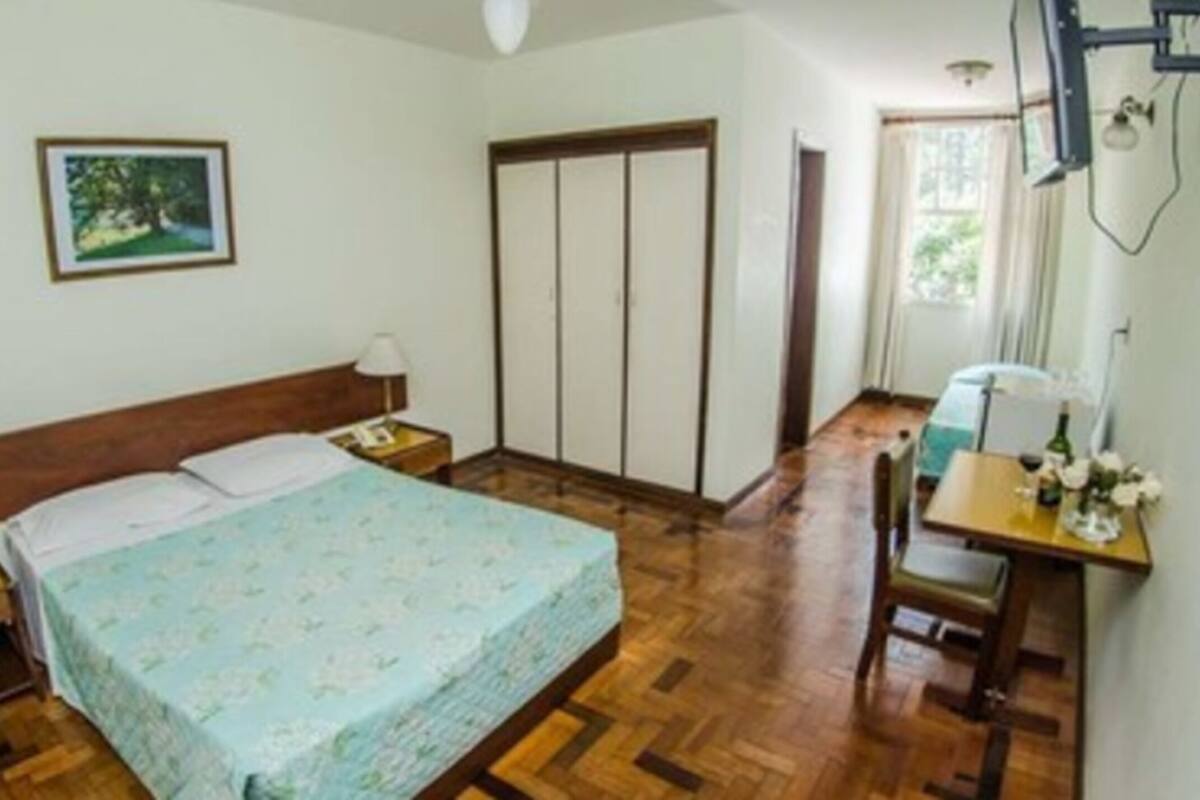 A bedroom with a bed, bedside tables, a desk, a chair, a wardrobe, and a window.