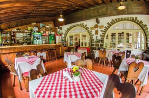A restaurant with red and white checkered tablecloths, wooden chairs, and a bar area with shelves of bottles.