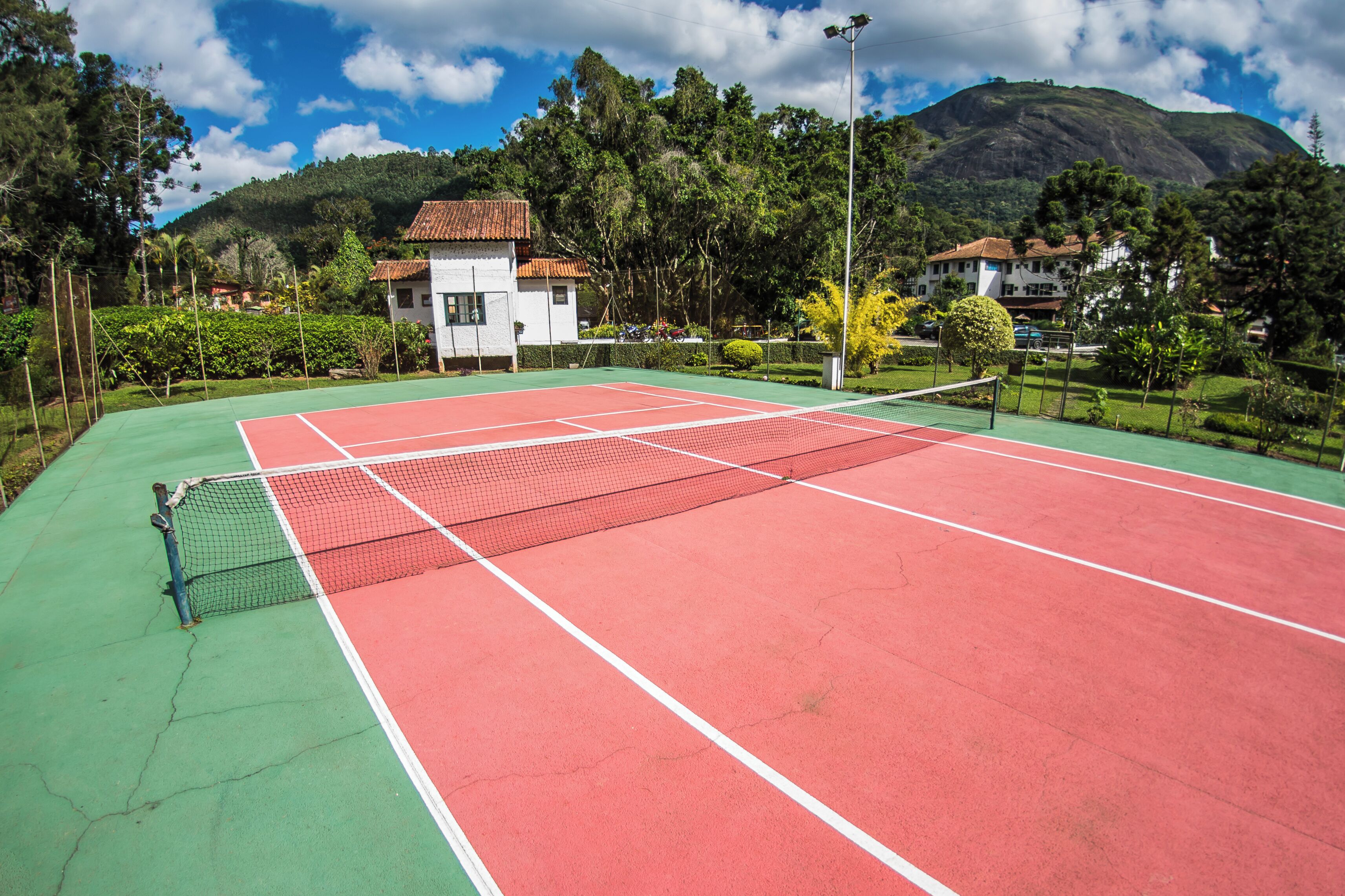 Una cancha de tenis con una red, rodeada de zonas verdes y casas.