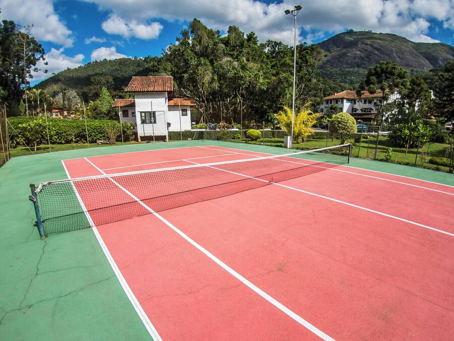 Una cancha de tenis con una red, rodeada de zonas verdes y casas.