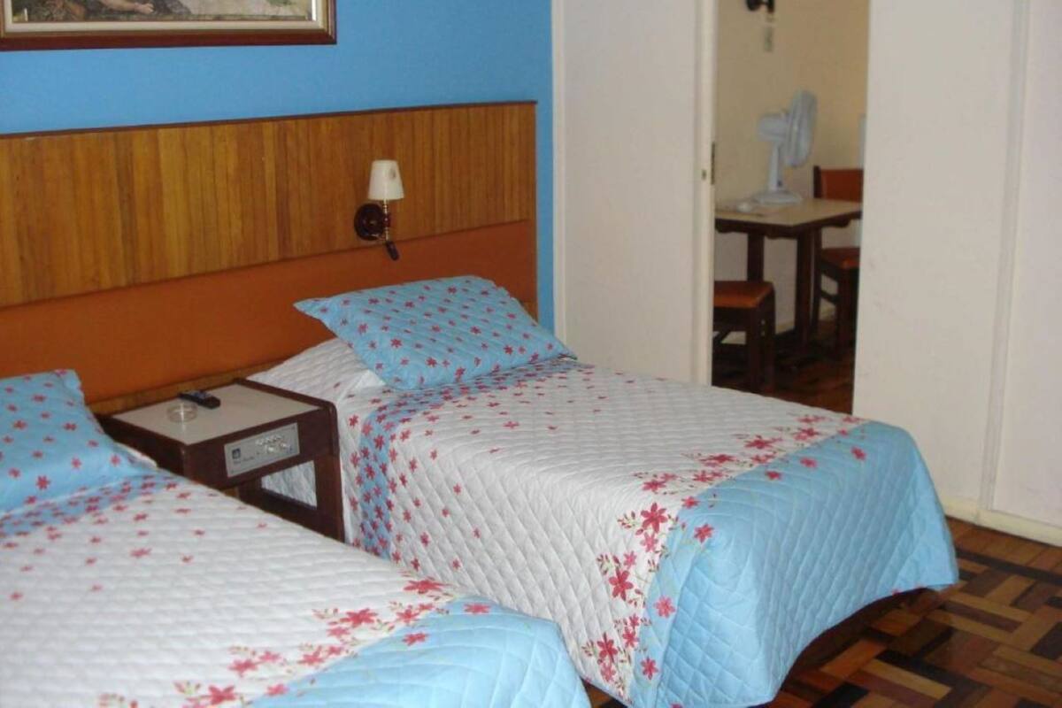 A hotel room with two beds, a wooden headboard, a nightstand, a lamp, and a painting on the wall.