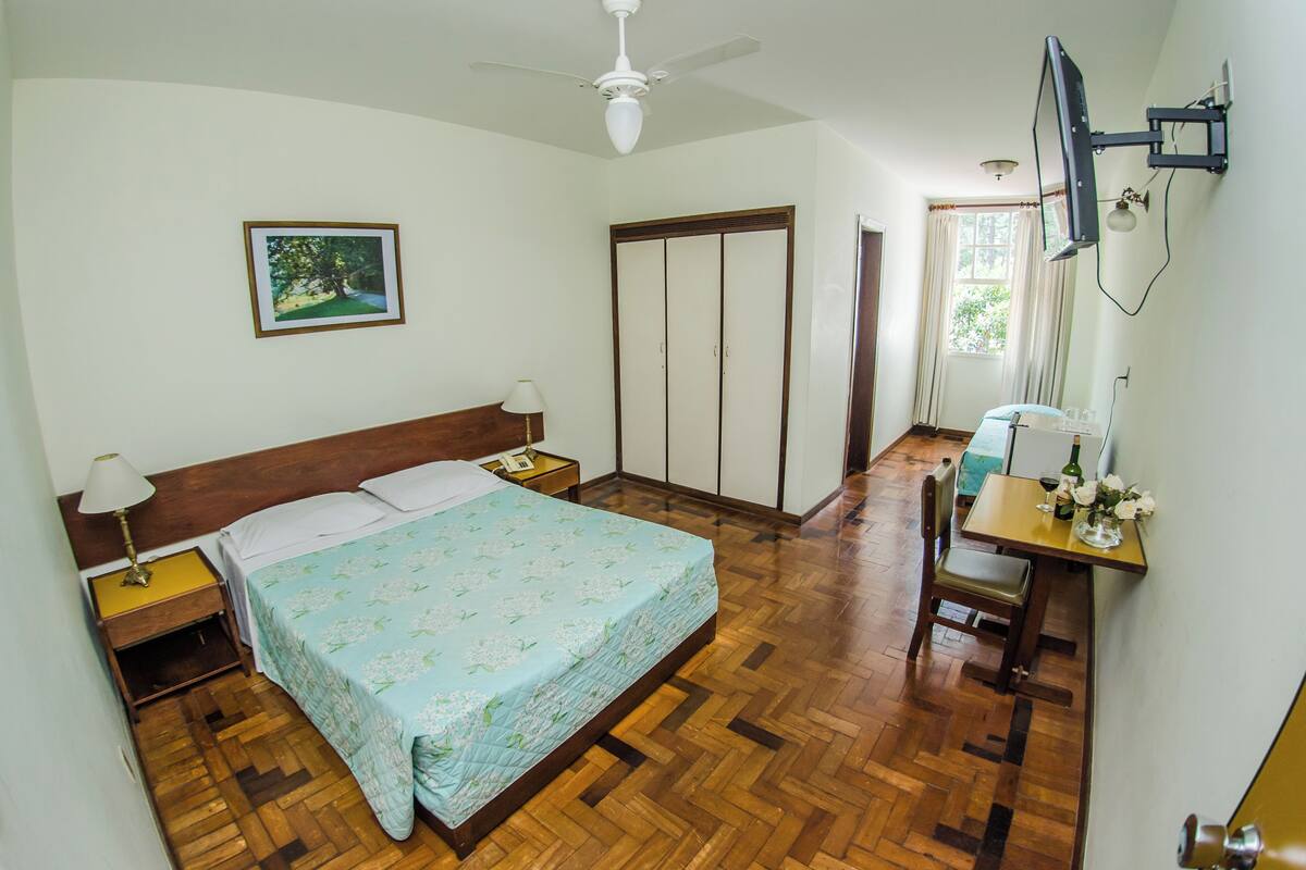 A bedroom with a bed, bedside tables, a desk, a chair, a television, and a wardrobe.