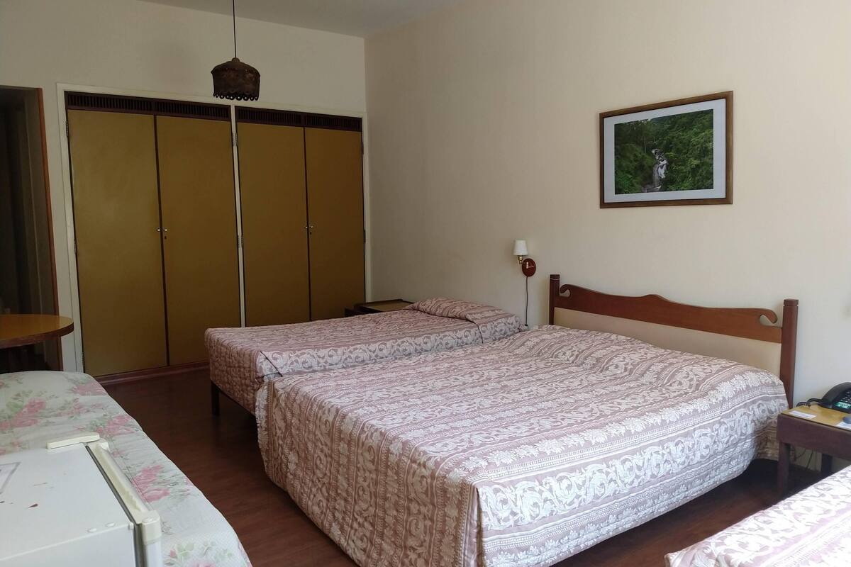 A bedroom with two beds, a wardrobe, a bedside table, a lamp, and a framed picture on the wall.