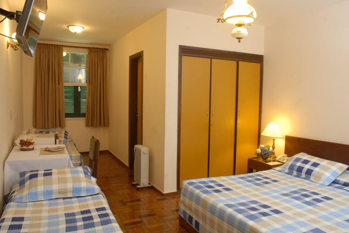 A hotel room with two beds, a dining table, a radiator, a wardrobe, and a television.