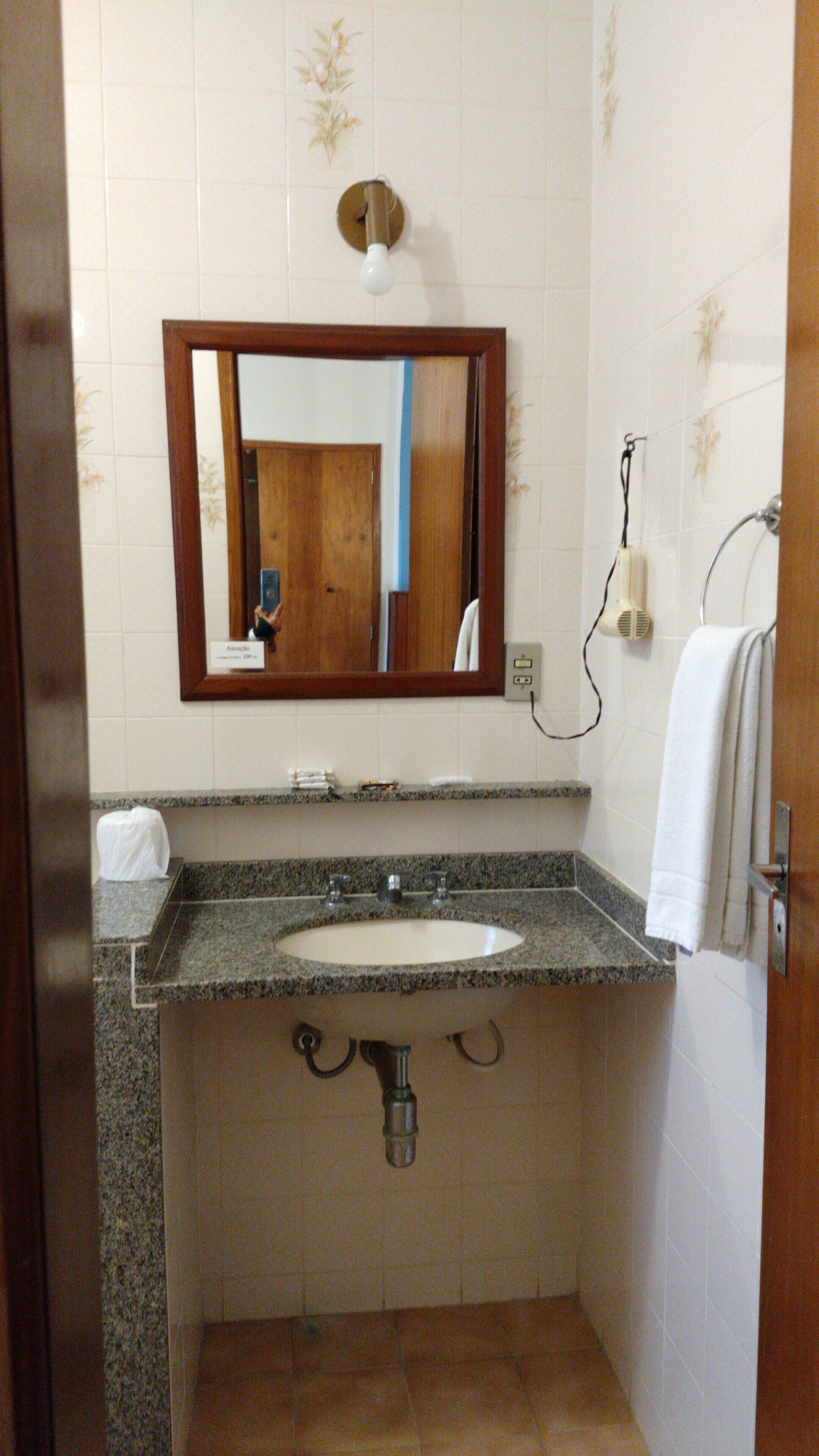 A bathroom with a sink, mirror, towel rack, and a hairdryer plugged in.