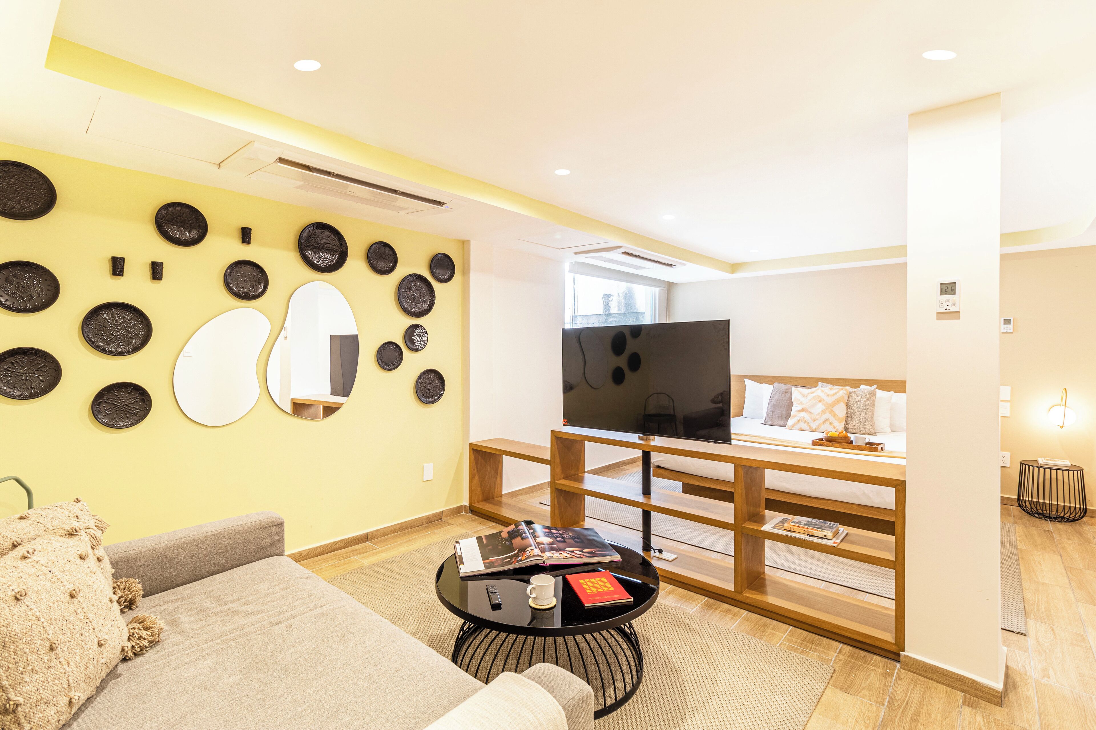 A modern living room with a sofa, a coffee table with books and a remote, a TV, and a wooden bench.