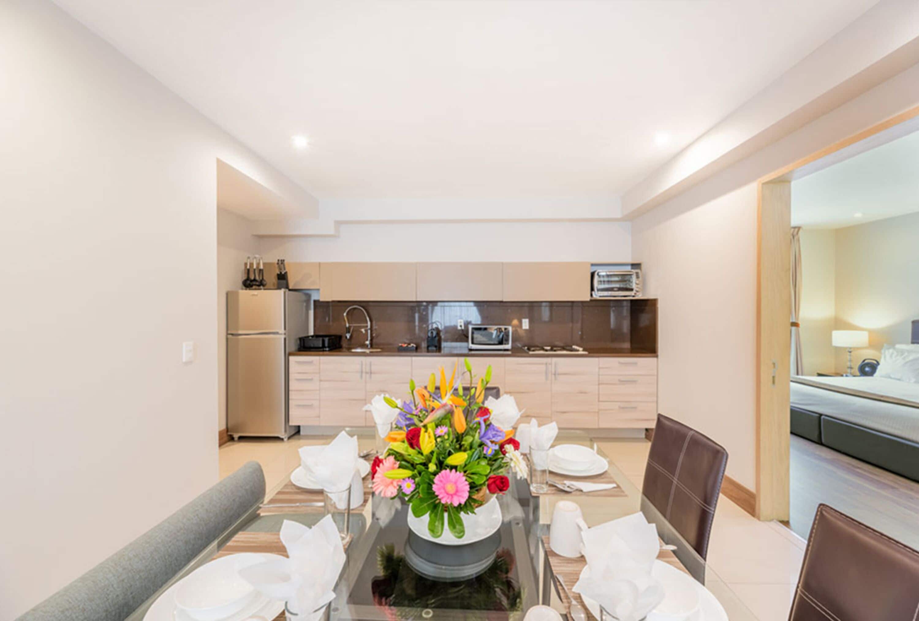Un comedor moderno con una mesa de vidrio, manteles blancos y un centro de mesa floral.