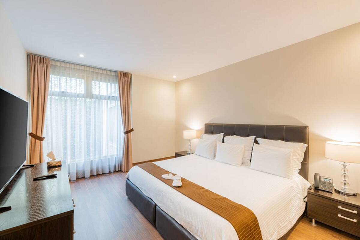 Habitació d'hotel amb un llit gran, televisió, escriptori i finestra amb cortines.