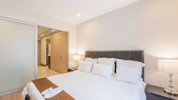 Habitación de hotel con una cama grande, piso de madera, armario con puerta corredera y mesita de noche con lámpara.