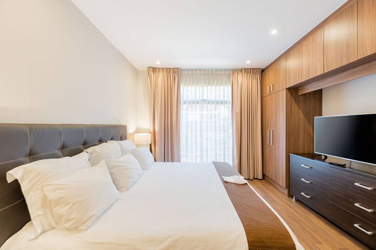 Habitació d'hotel amb un llit gran, televisió, armaris de fusta i una finestra amb cortines.