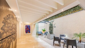 Un vestíbulo moderno con suelo de mármol, pared de vidrio y zona de estar con sillas y una mesa.