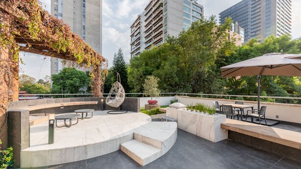 Un patio al aire libre con asientos, una silla colgante y una pérgola cubierta de enredaderas.