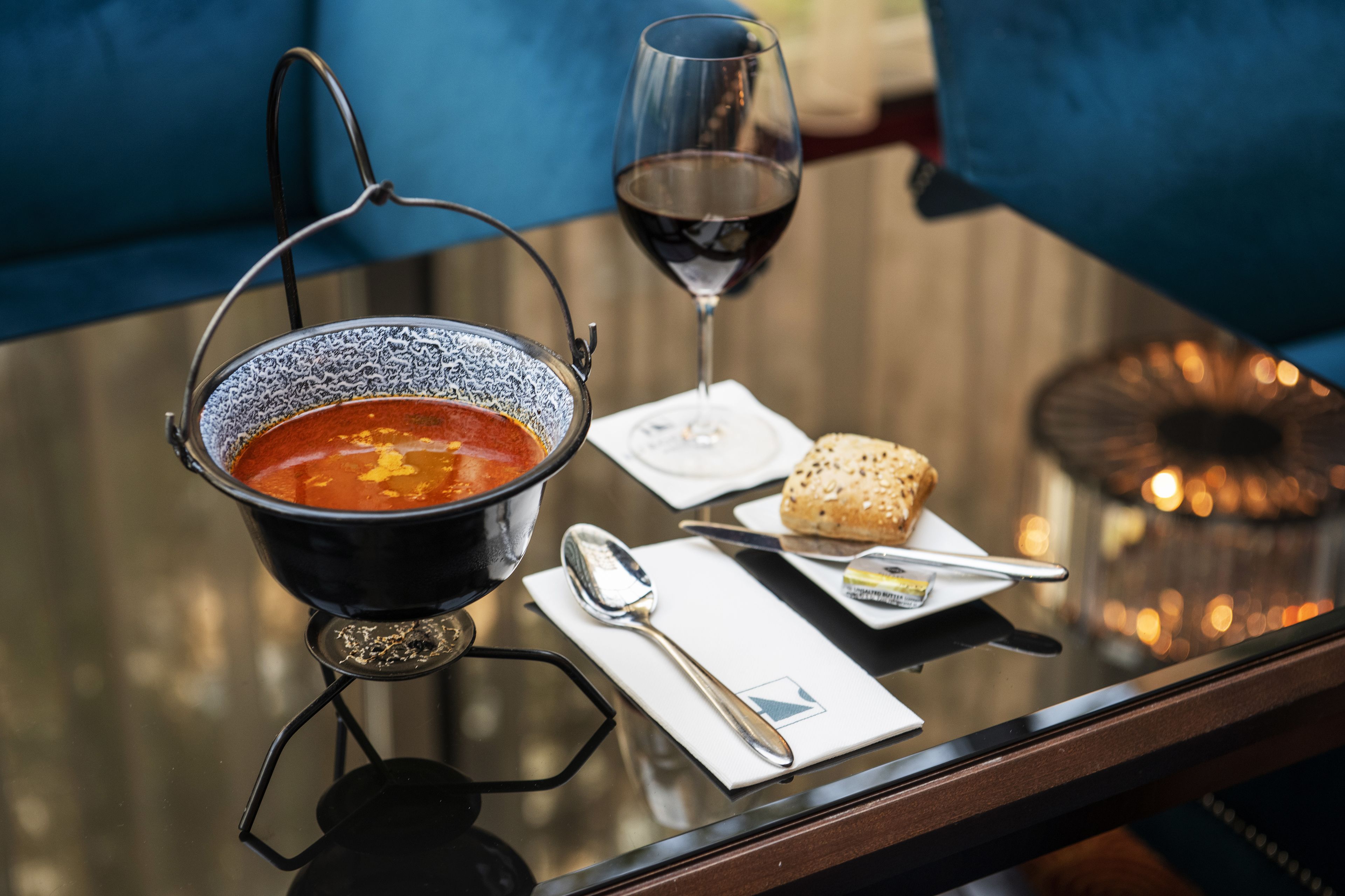Una mesa con un tazón de sopa, una copa de vino tinto, un trozo de pan y una cuchara.
