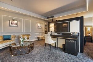 A modern hotel room with a sofa, a small coffee table, a chair, a desk, and a mini-fridge.