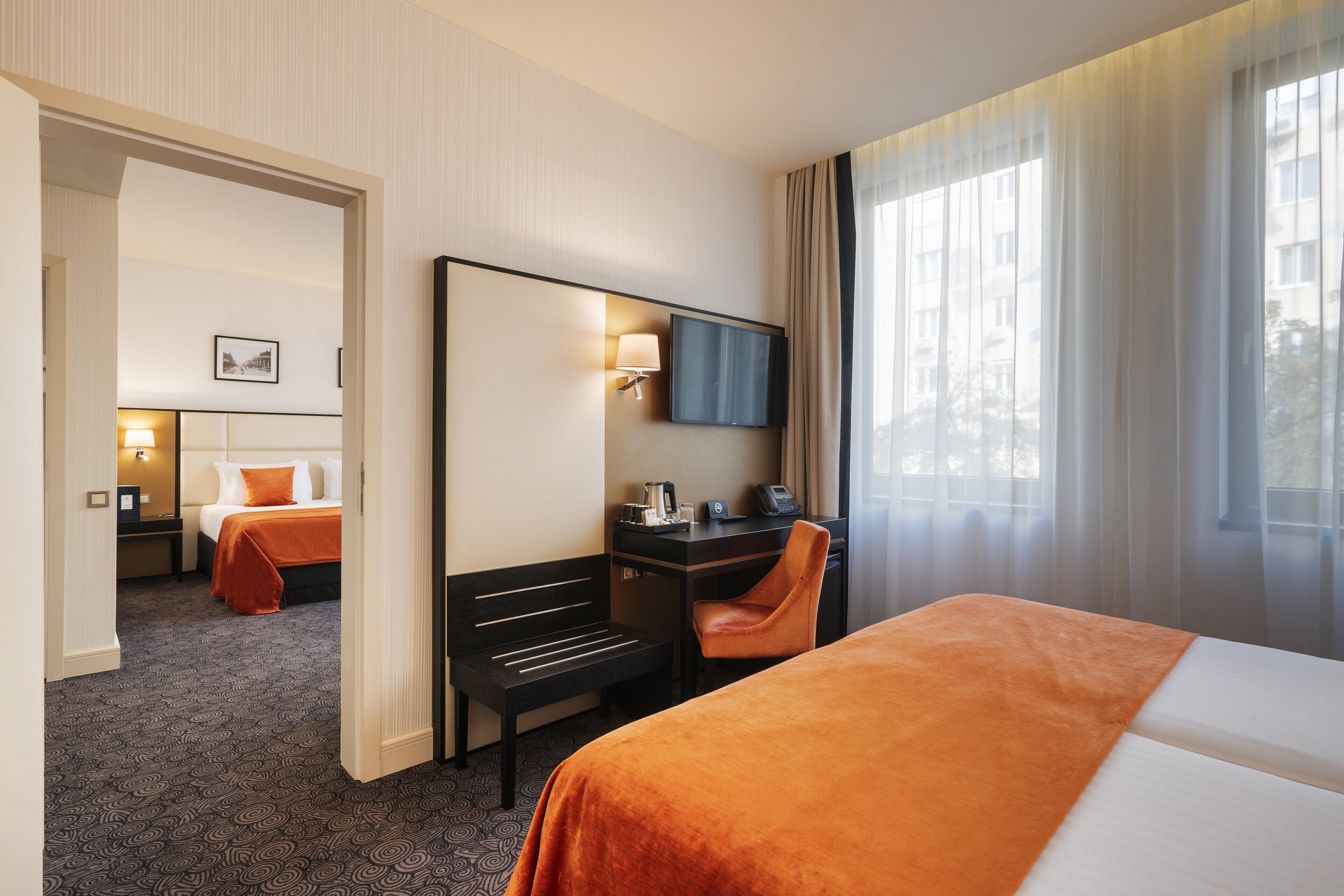 A hotel room with a bed, desk, chair, and a large mirror.