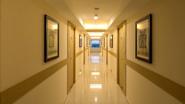 Een hotelgang met ingelijste kunstwerken aan de muren, een gepolijste vloer en een heldere plafondlamp.