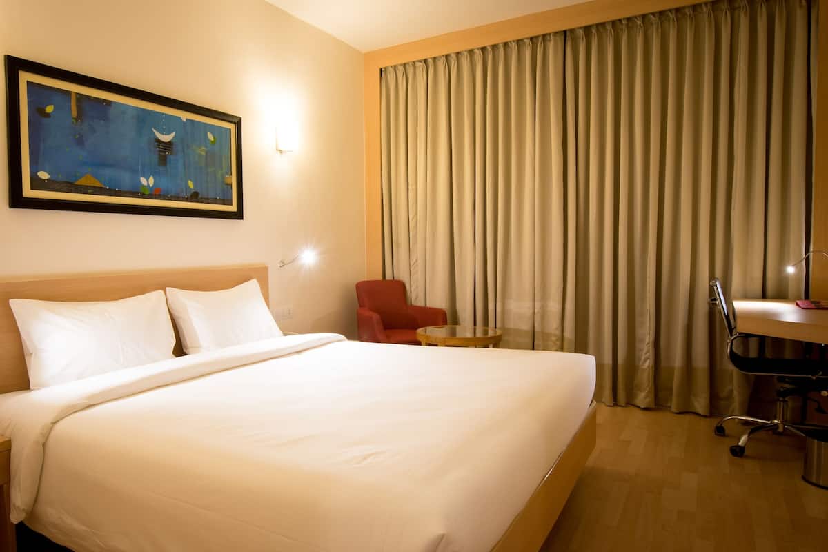 Een hotelkamer met een groot bed, een bureau met stoel, een klein tafeltje en een schilderij aan de muur.
