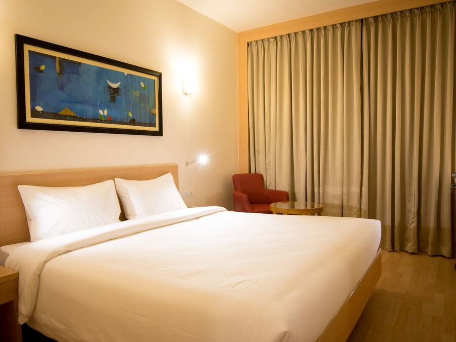 A hotel room with a large bed, a desk with a chair, a small table, and a painting on the wall.