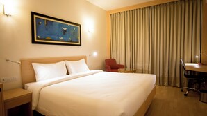 Een hotelkamer met een groot bed, een bureau, een stoel, een kleine tafel en een schilderij aan de muur.