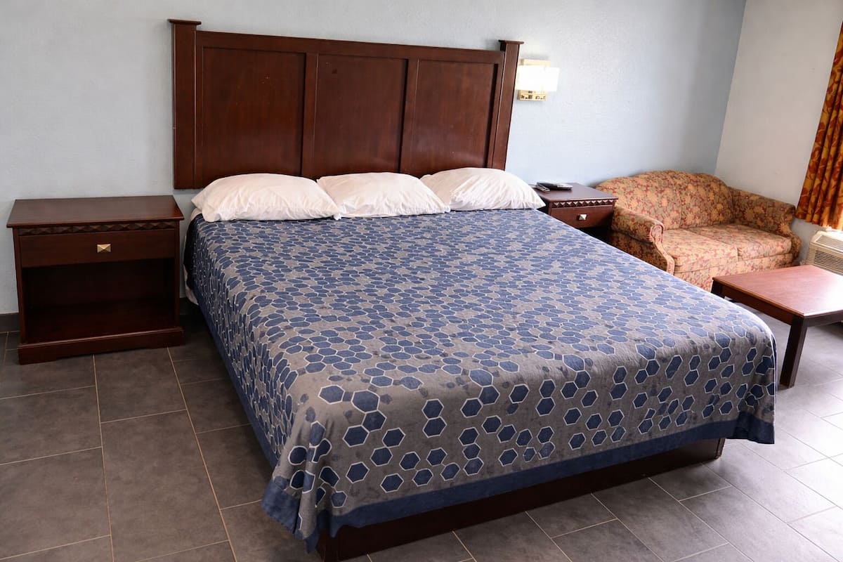 A hotel room with a large bed, a nightstand, a chair, and a small table.