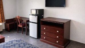 Habitación pequeña con cama, escritorio, silla, microondas, refrigerador, televisor y cómoda.