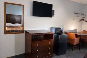 Habitación de hotel con una cama, cómoda, escritorio con silla, microondas y televisor montado en la pared.
