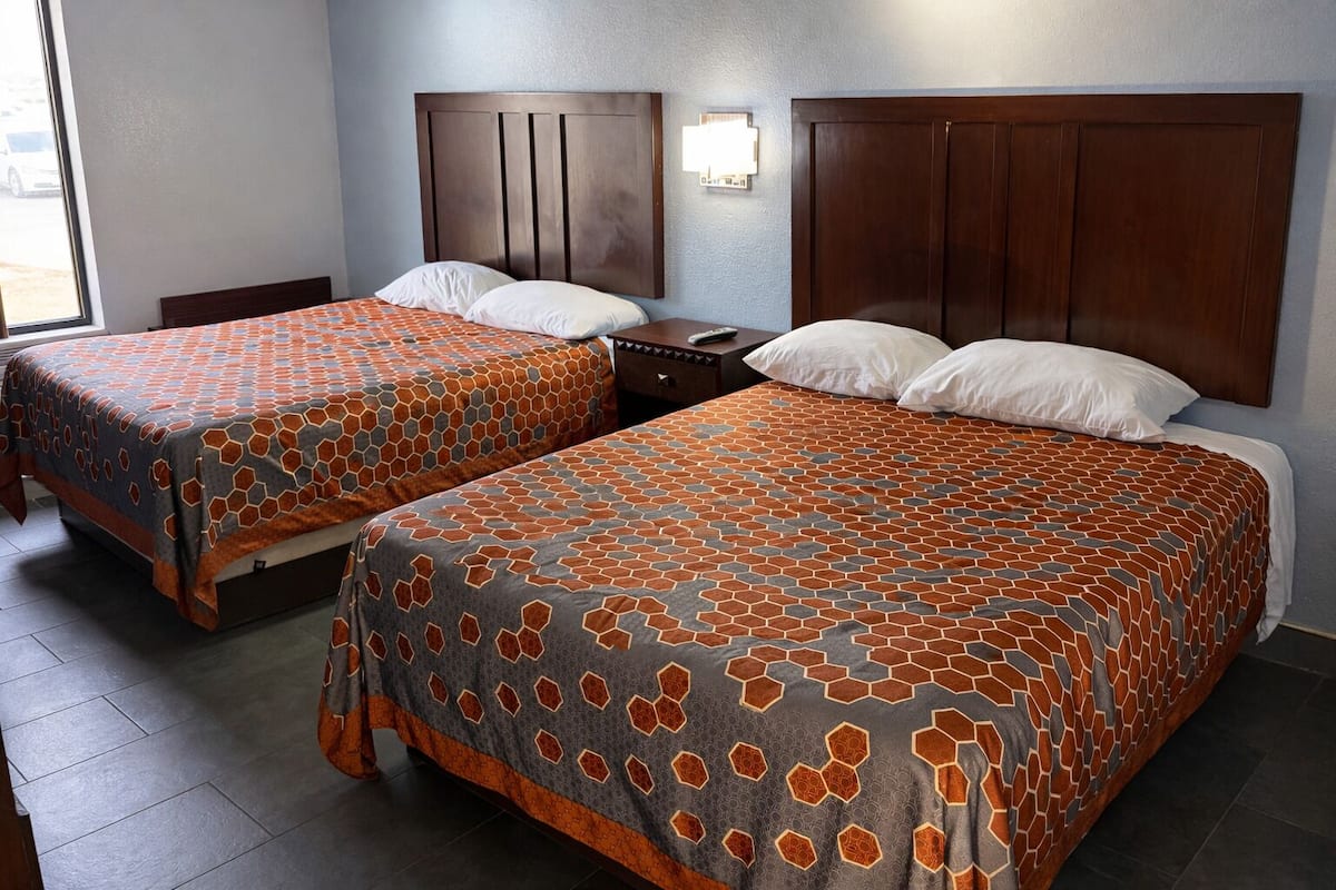 A hotel room with two beds, each with a patterned bedspread, a wooden headboard, and a nightstand with a lamp.