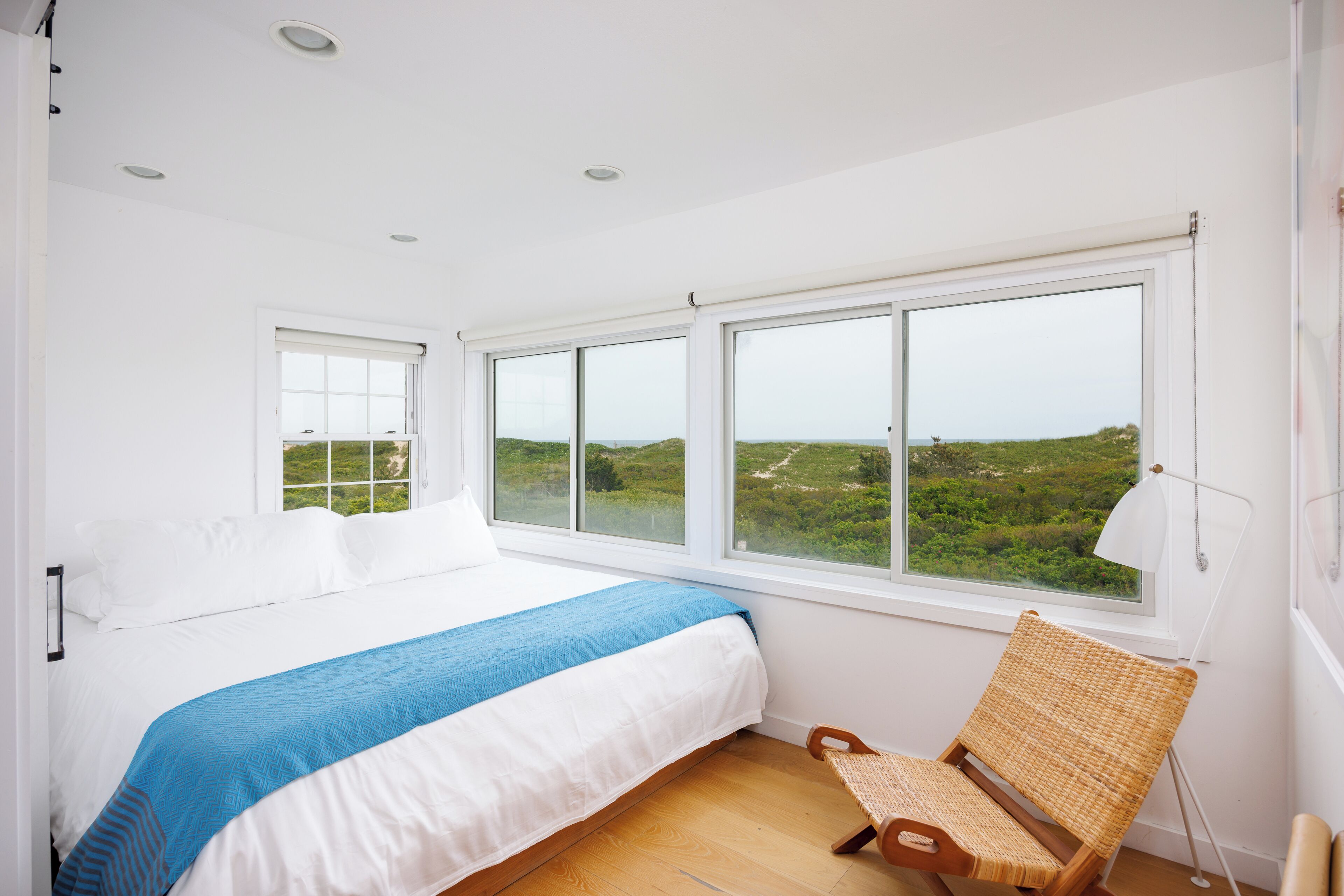 A bedroom with a large bed, a view of greenery outside, and a chair by the window.