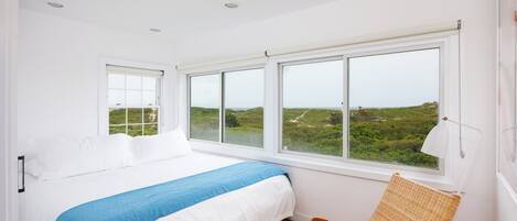 A bedroom with a large bed, a view of greenery outside, and a chair by the window.
