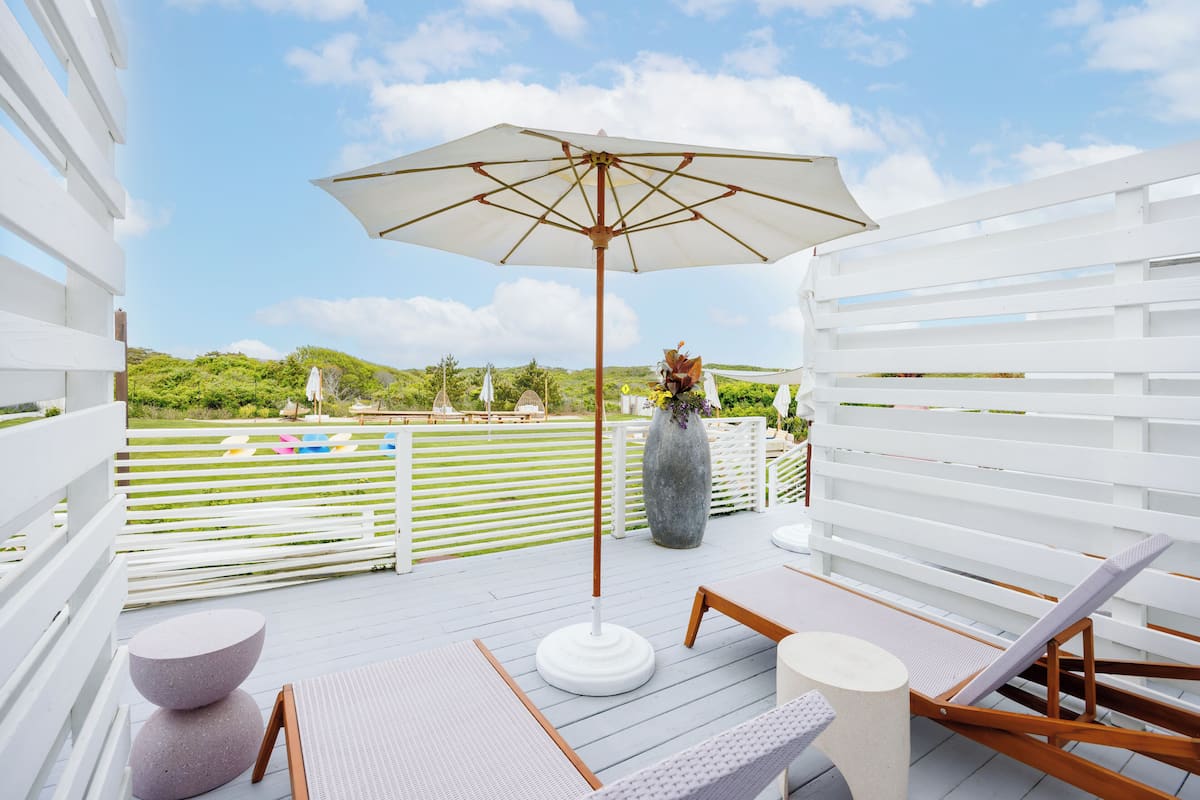 A deck with a white umbrella, seating, and a vase with flowers.