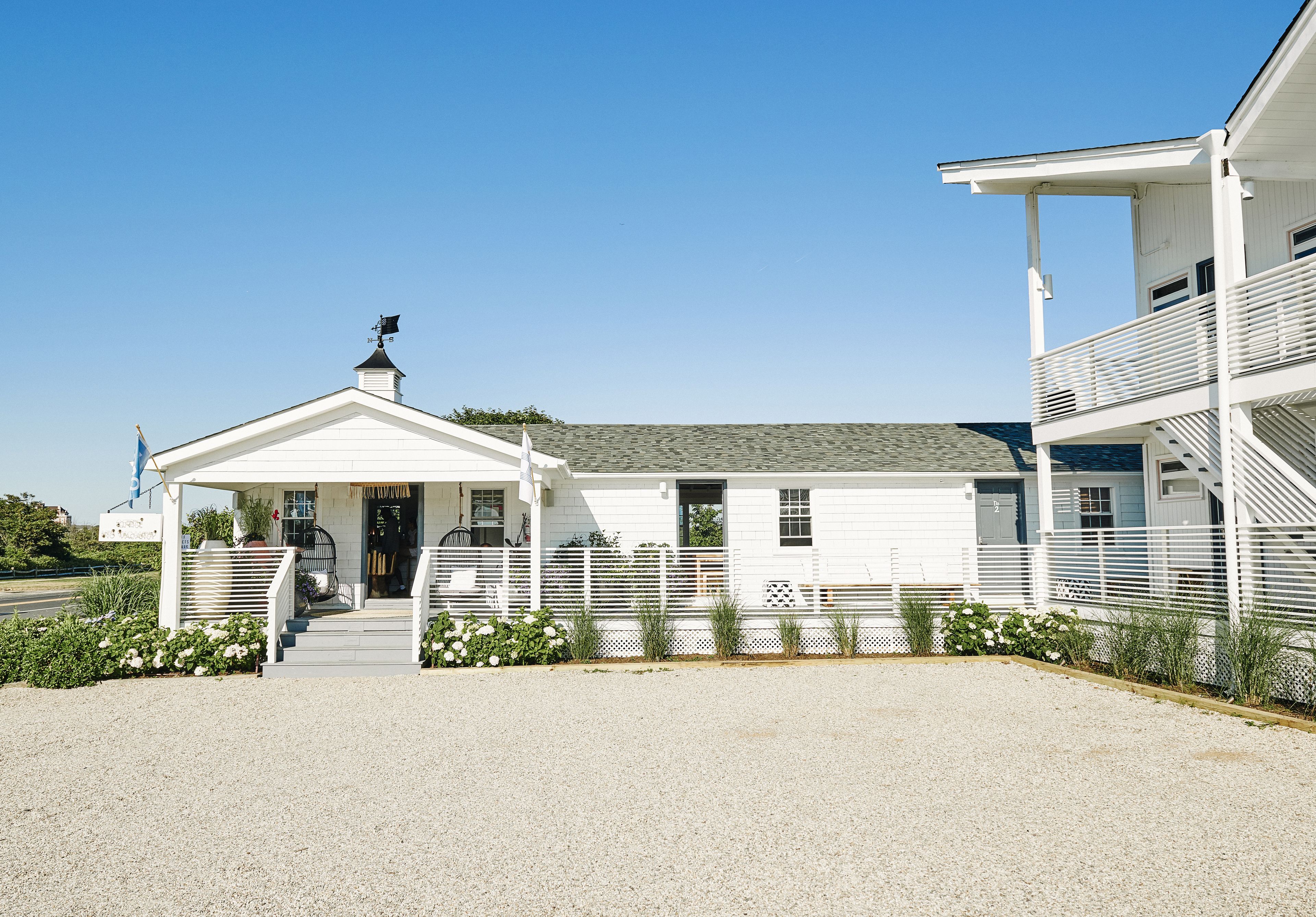 A white building with a covered entrance, a small porch, and a gravel driveway.