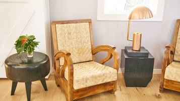 A wooden chair with a woven backrest, a round black side table with a plant, and a black cube-shaped side table with a lamp.