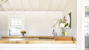A kitchen with a wooden countertop, three bar stools, a hanging light fixture, and a window with a view. - Hero Beach Club (Montauk)