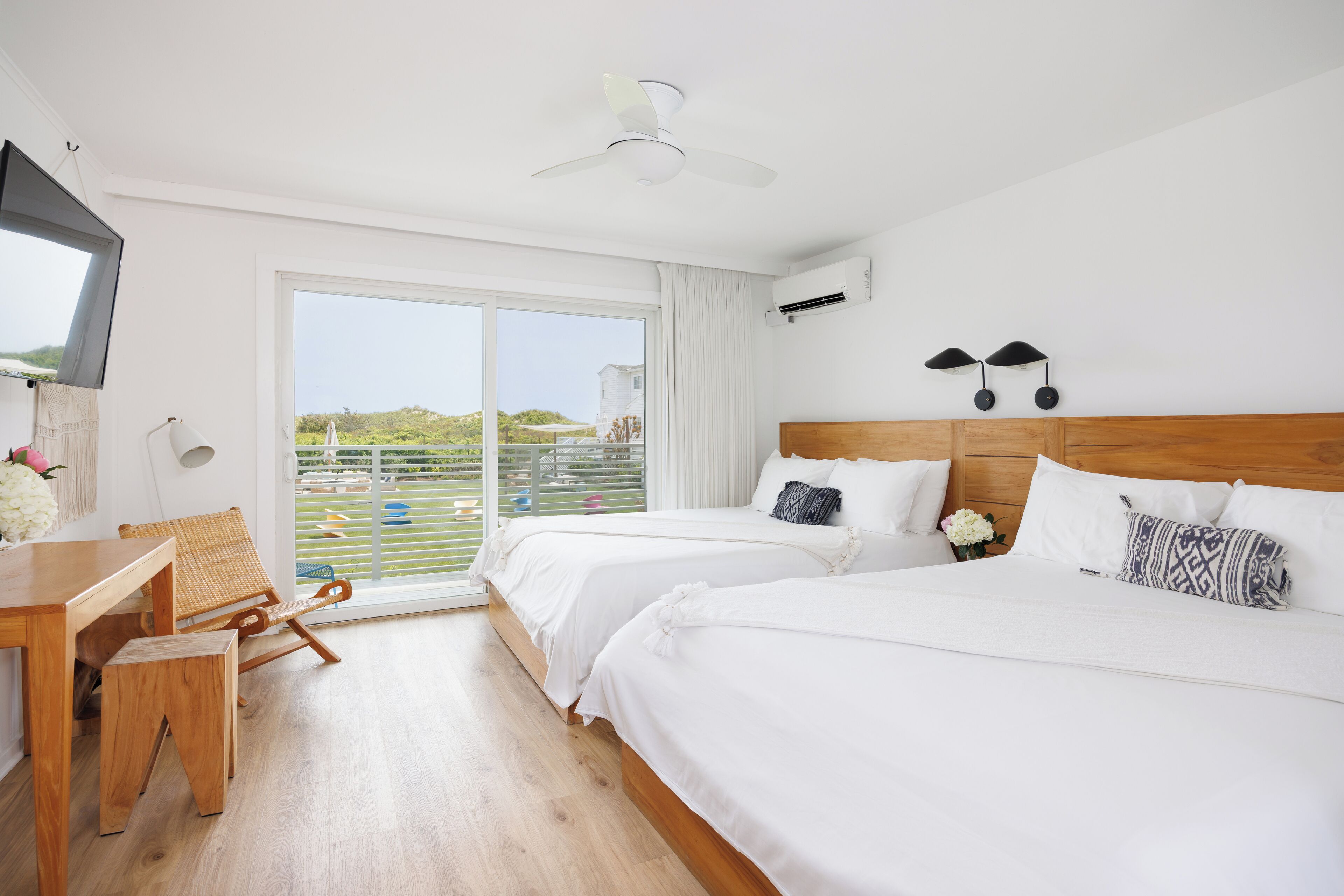 Habitación de hotel con dos camas, un escritorio de madera, una silla, un televisor y un balcón con vistas.