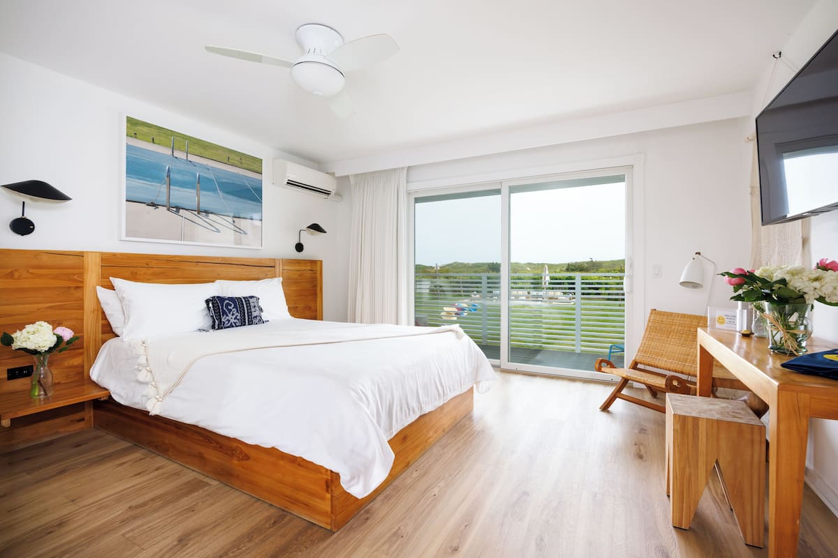 A bedroom with a wooden bed, a desk, a chair, a TV, and a balcony with a view.
