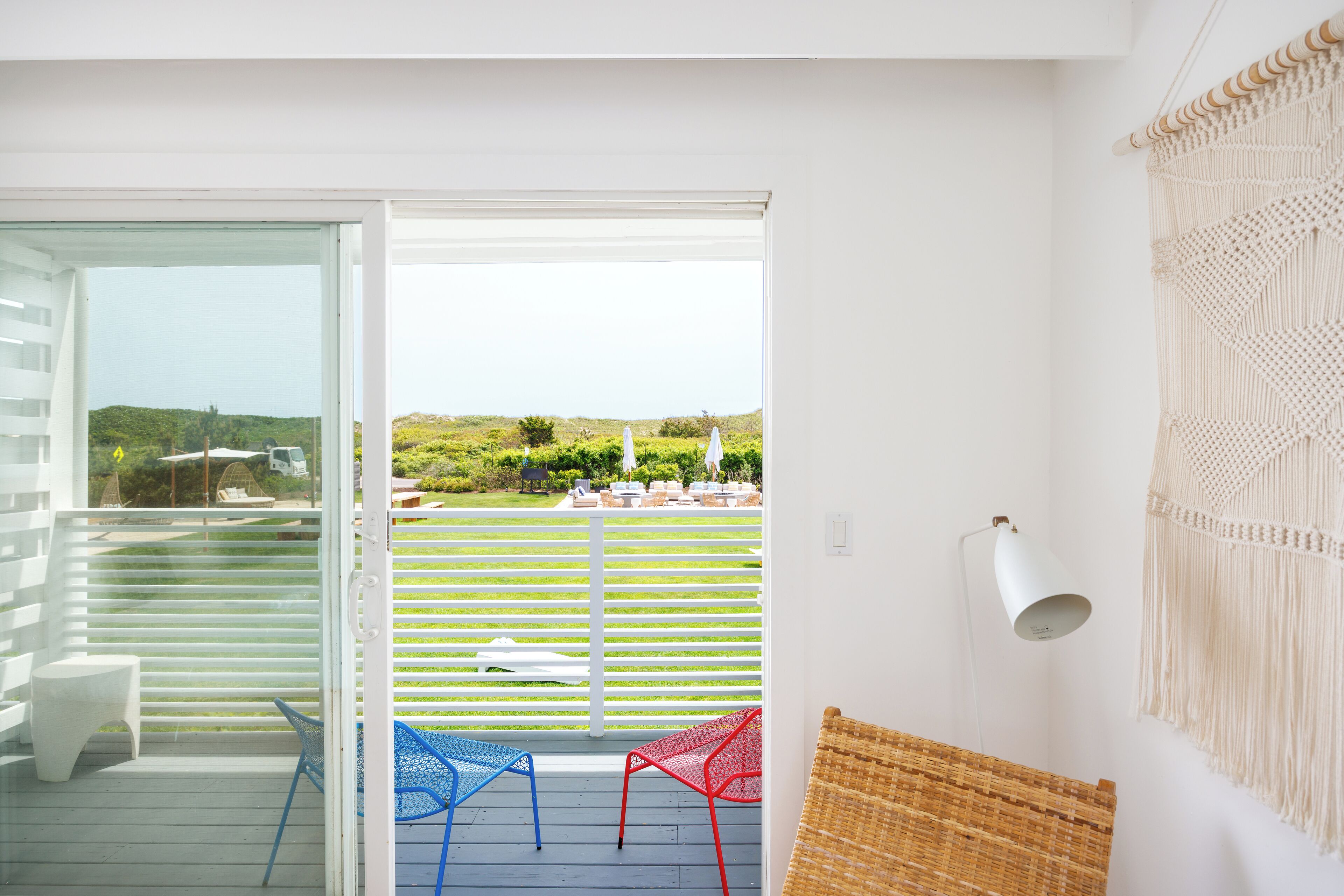 A balcony with a view of a green landscape, white railings, and a macrame wall hanging.