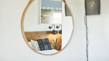 A bedroom with a wooden headboard, a bed with white and patterned pillows, a hanging light fixture, and a framed picture on the wall.