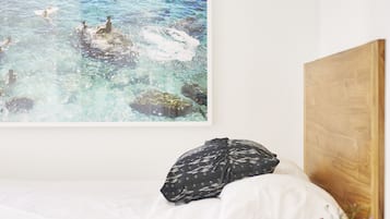 A bedroom with a bed, a wooden headboard, a wall-mounted painting of a beach scene, and a small wooden nightstand with a vase of flowers.