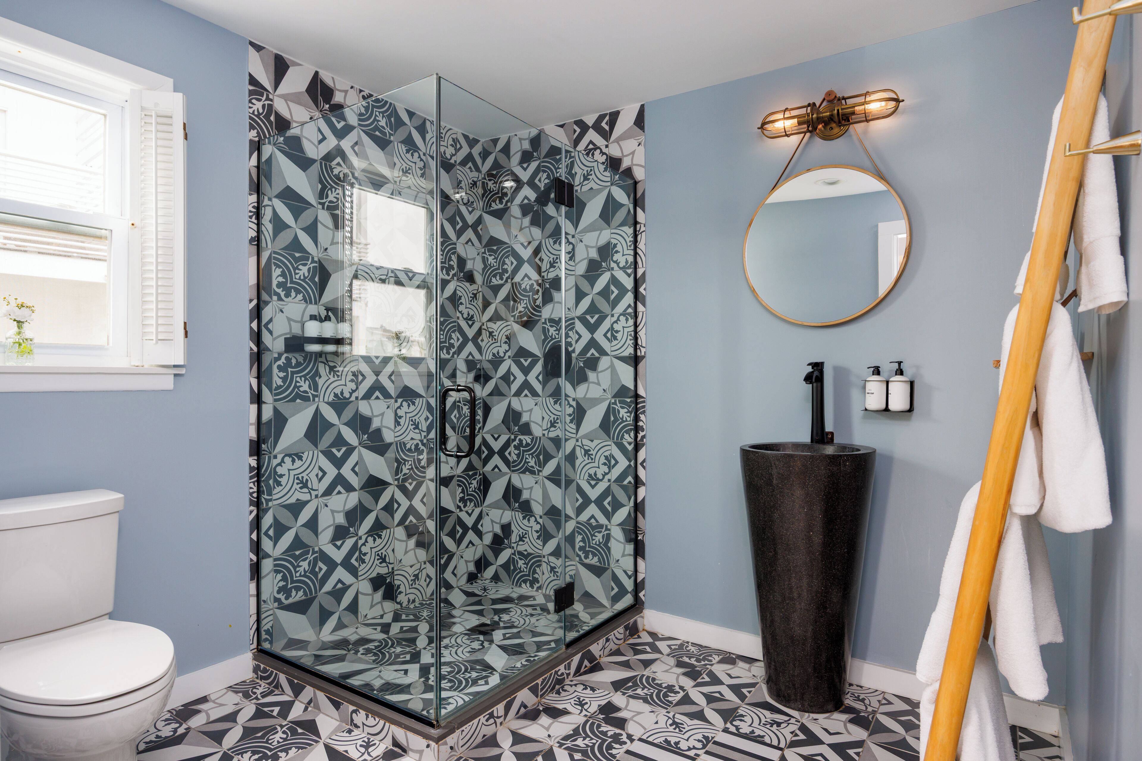 A bathroom with a glass shower enclosure, a sink with a black basin, and a mirror on the wall.