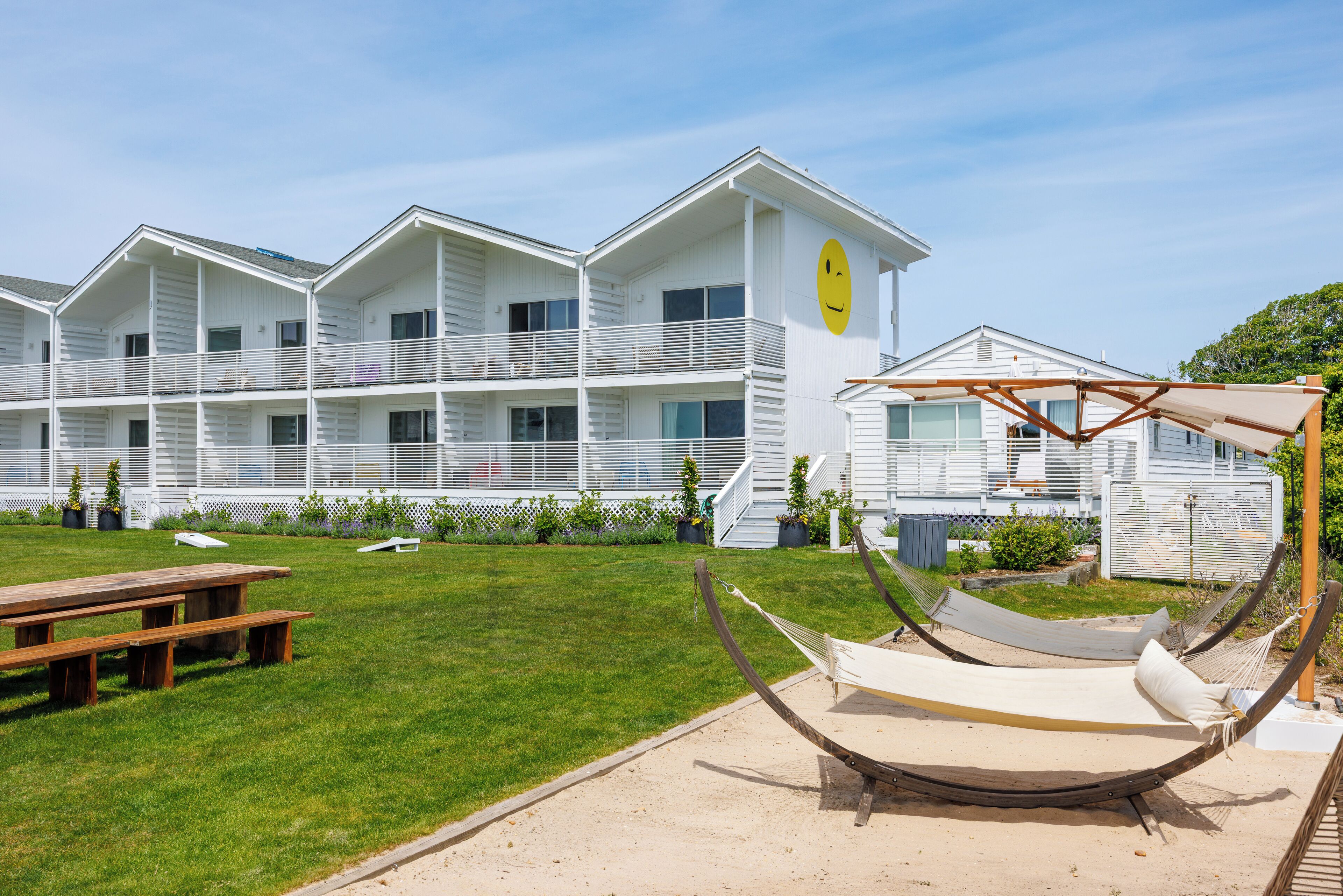 A multi-story building with a white exterior, a balcony, and a yellow smiley face on the side.