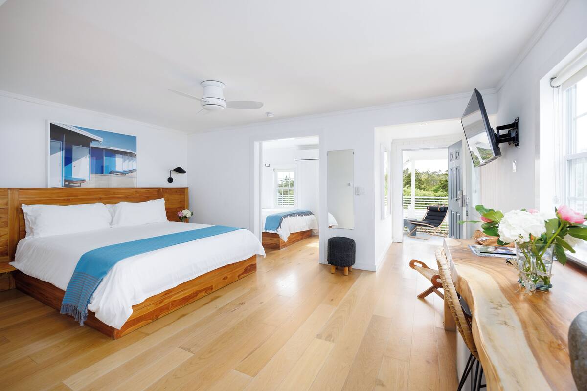 A spacious bedroom with a large bed, a wooden headboard, a small stool, and a wooden bench.