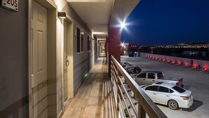 A hotel corridor with a view of parked cars and a cityscape at night.