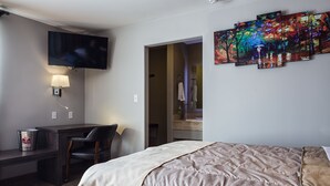 A hotel room with a bed, desk, chair, TV, and a painting on the wall.