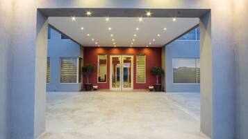 A modern building entrance with a concrete floor, two potted plants, and a glass door.