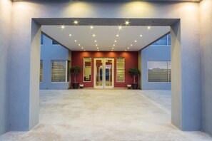 A modern building entrance with a concrete floor, two potted plants, and a glass door.
