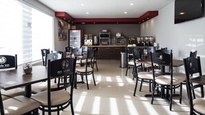 A modern dining area with multiple tables and chairs, a kitchen area with appliances, and a large TV mounted on the wall.