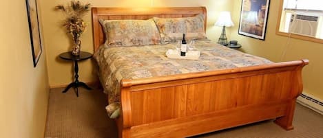 A wooden bed with a floral bedspread, a small table with a vase, and a poster on the wall.