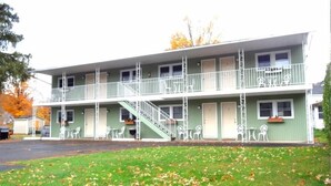 Un motel de dos pisos con una escalera central, balcones y un jardín delantero cubierto de césped.